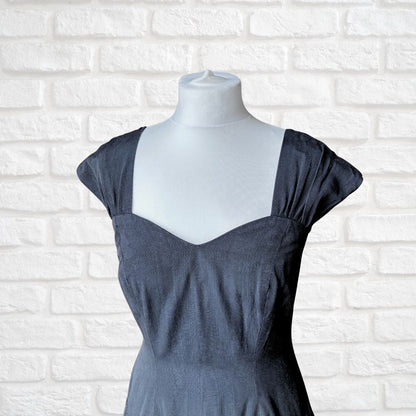 A black sleeveless dress displayed on a white mannequin torso against a white brick wall background.