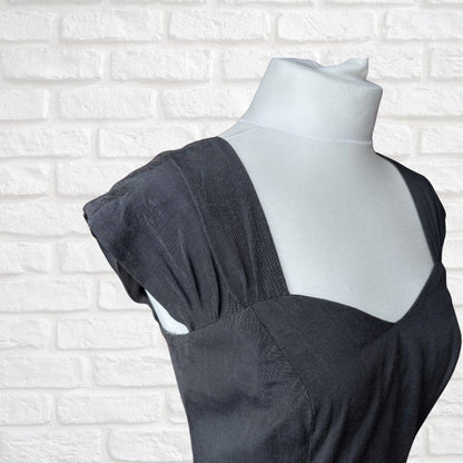 A black textured dress displayed on a white mannequin torso against a white brick wall background.
