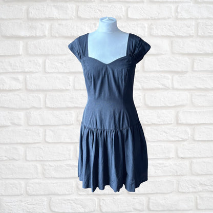 A black tiered mini dress with cap sleeves and a scoop neckline, displayed on a light blue mannequin torso against a white brick wall background.