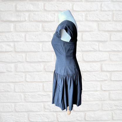 A black  tiered dress displayed on a mannequin torso against a white brick wall background.