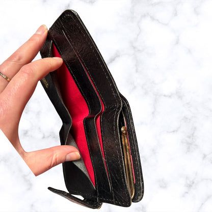 Hand holding an open black wallet with a red interior against a white marble background