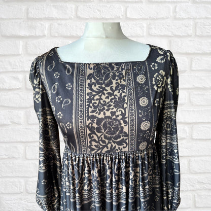 Black patterned dress on a mannequin against a white brick wall.