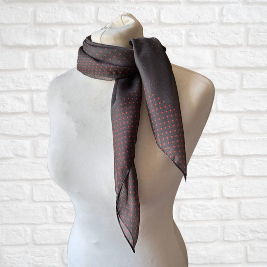 Mannequin wearing a dark gray scarf with red polka dots against a white brick wall.