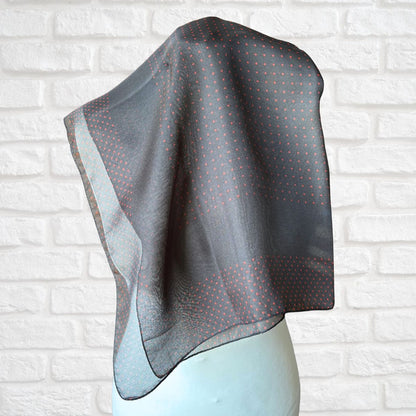 Black patterned scarf draped over a mannequin against a white brick wall.