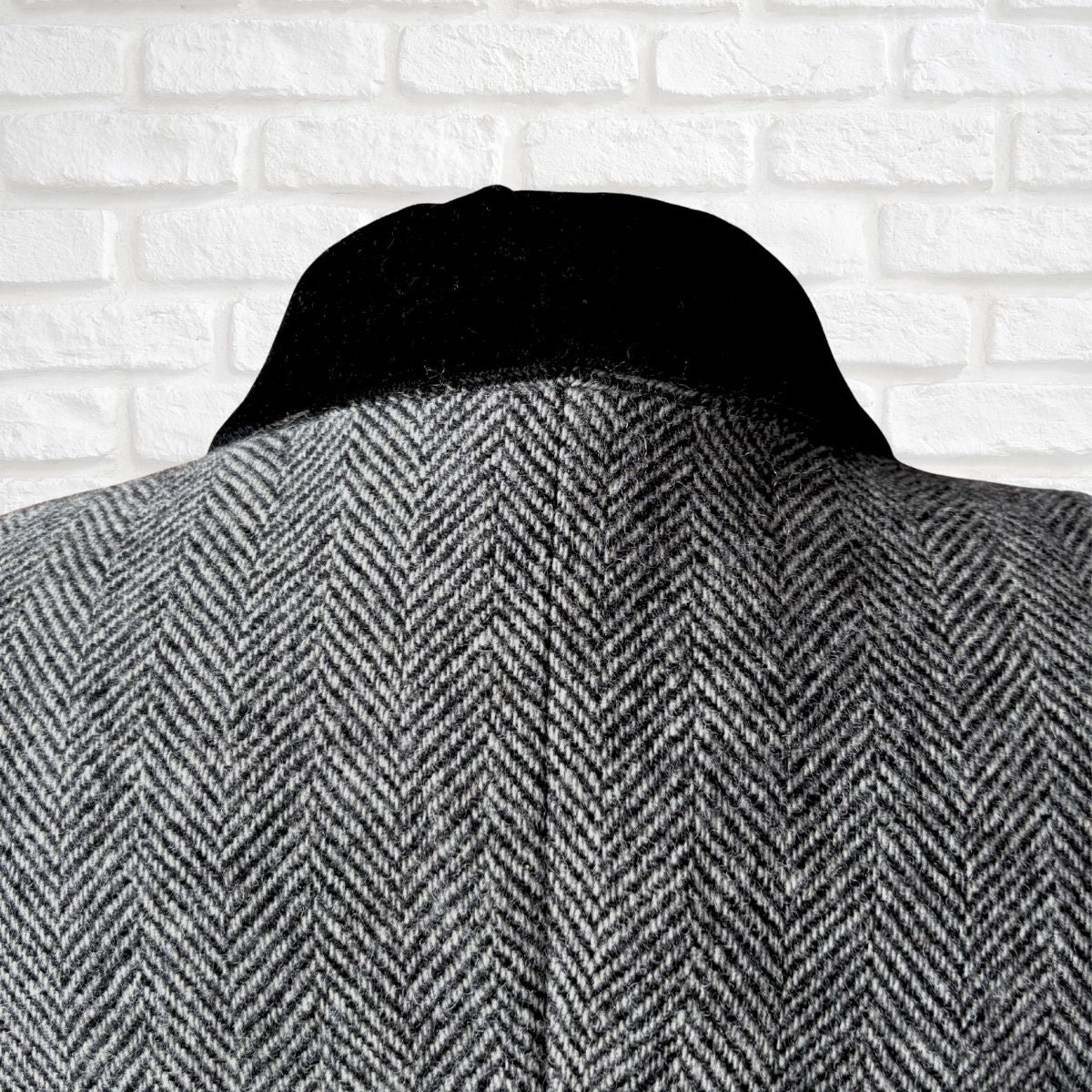 Black and white  herringbone patterned coat against a white brick wall background