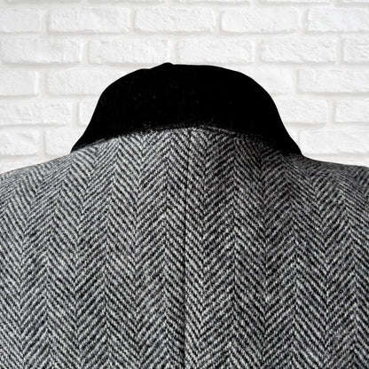 Black and white  herringbone patterned coat against a white brick wall background
