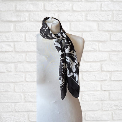 Black and white patterned scarf on a mannequin against a white brick wall.