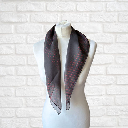 Mannequin wearing a dark gray scarf with subtle pattern against a white brick wall.