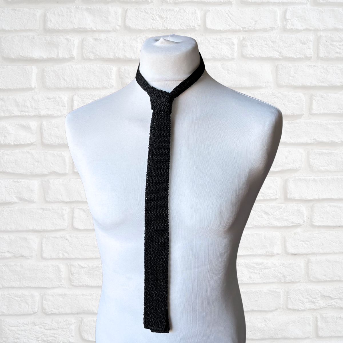 Black tie on a mannequin against a white brick wall background