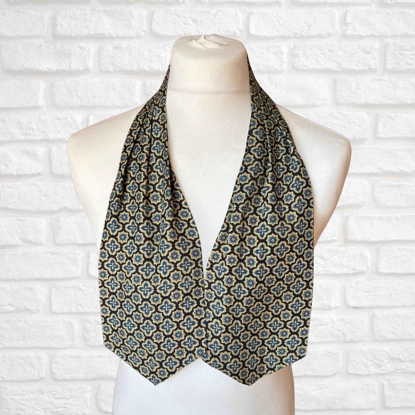 A vintage Austin Reed cravat featuring a black necktie with a cream, gold, and blue stylized floral print, displayed on a mannequin against a white brick wall background.