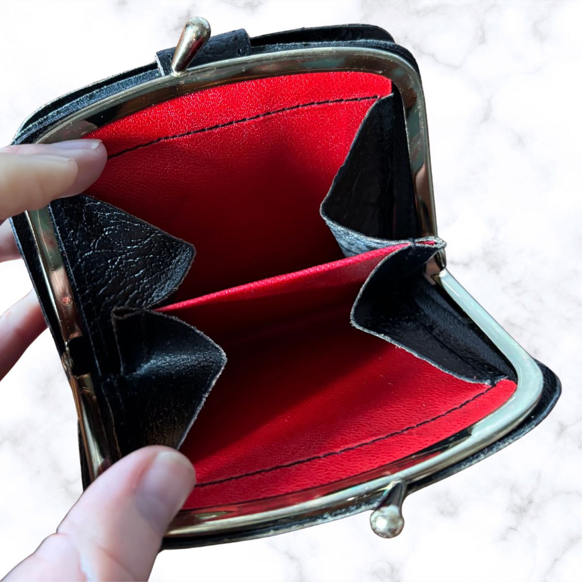 Open red wallet with black interior and decorative bow held by a hand on a light background