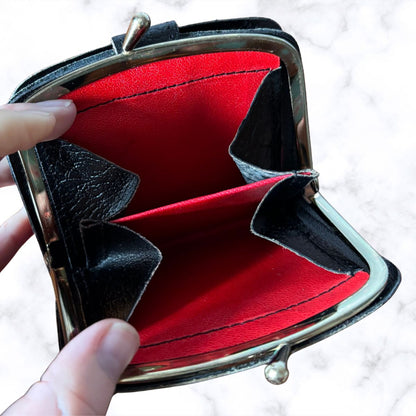 Open red wallet with black interior and decorative bow held by a hand on a light background
