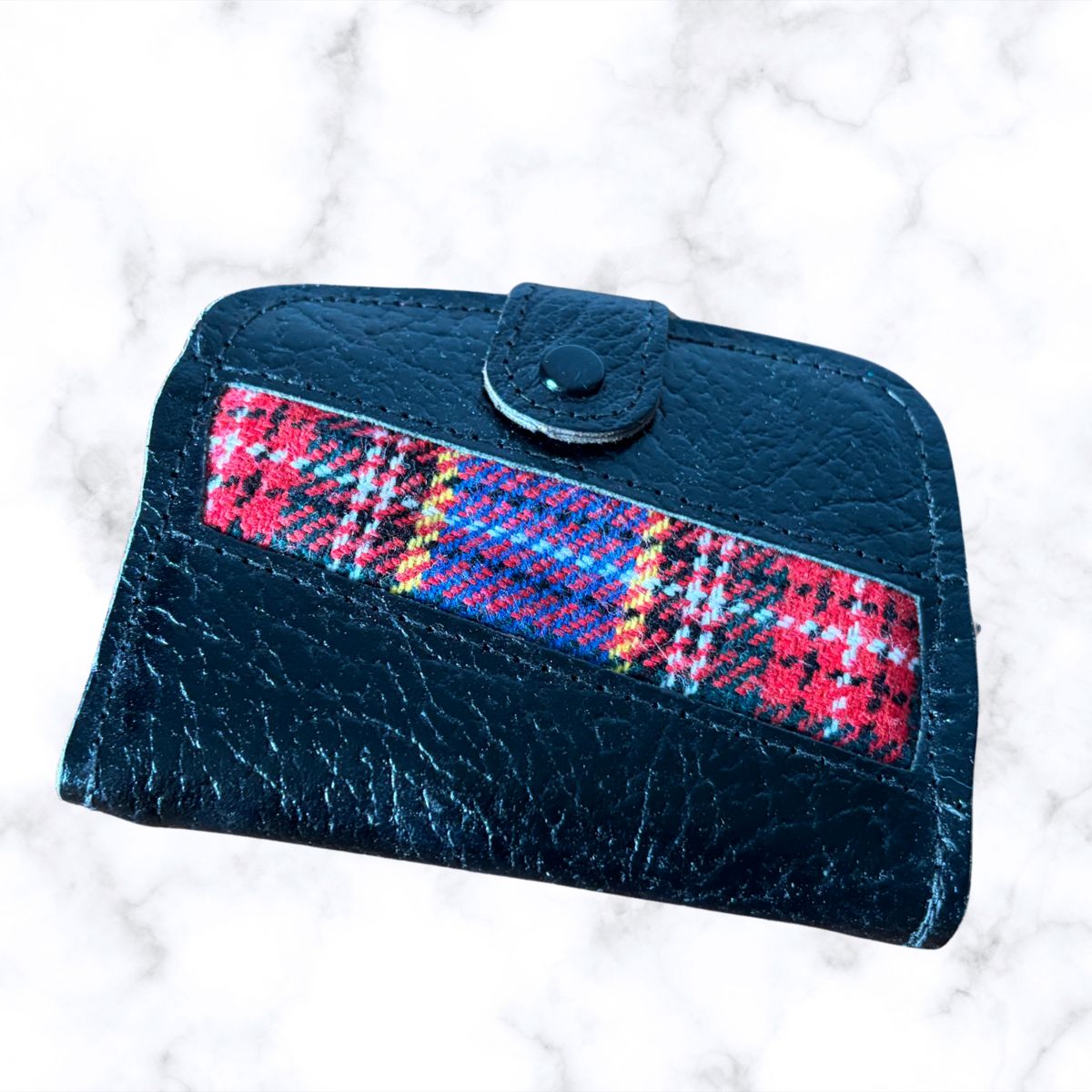 Black wallet with a plaid strap on a white marble background