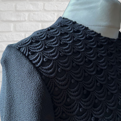 Textured fabric with scalloped edge on a mannequin against a white brick wall.