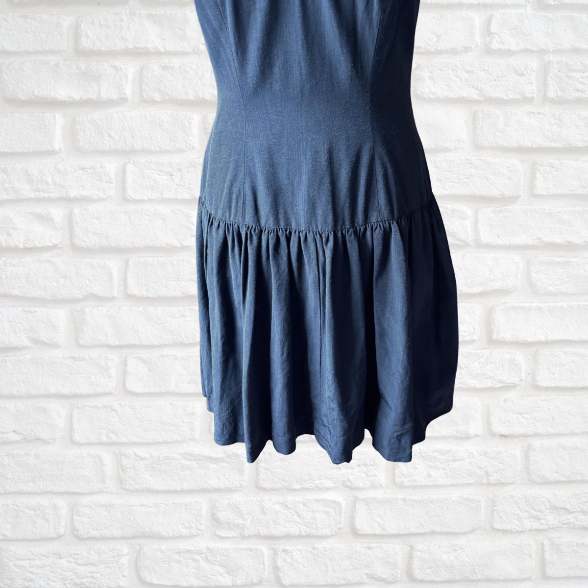 A sleeveless black dress displayed on a mannequin torso against a white painted brick wall background.