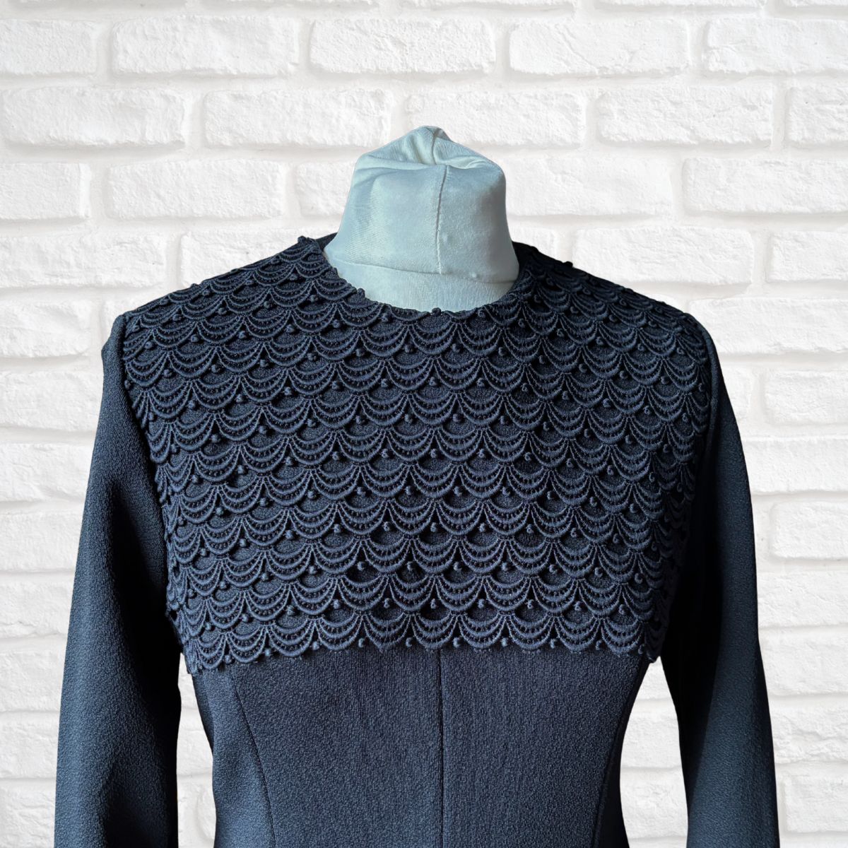 Dark blue textured garment with a patterned shoulder section on a white brick wall background