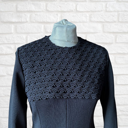 Dark blue textured garment with a patterned shoulder section on a white brick wall background