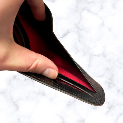Hand holding a leather wallet with red interior on a white textured background