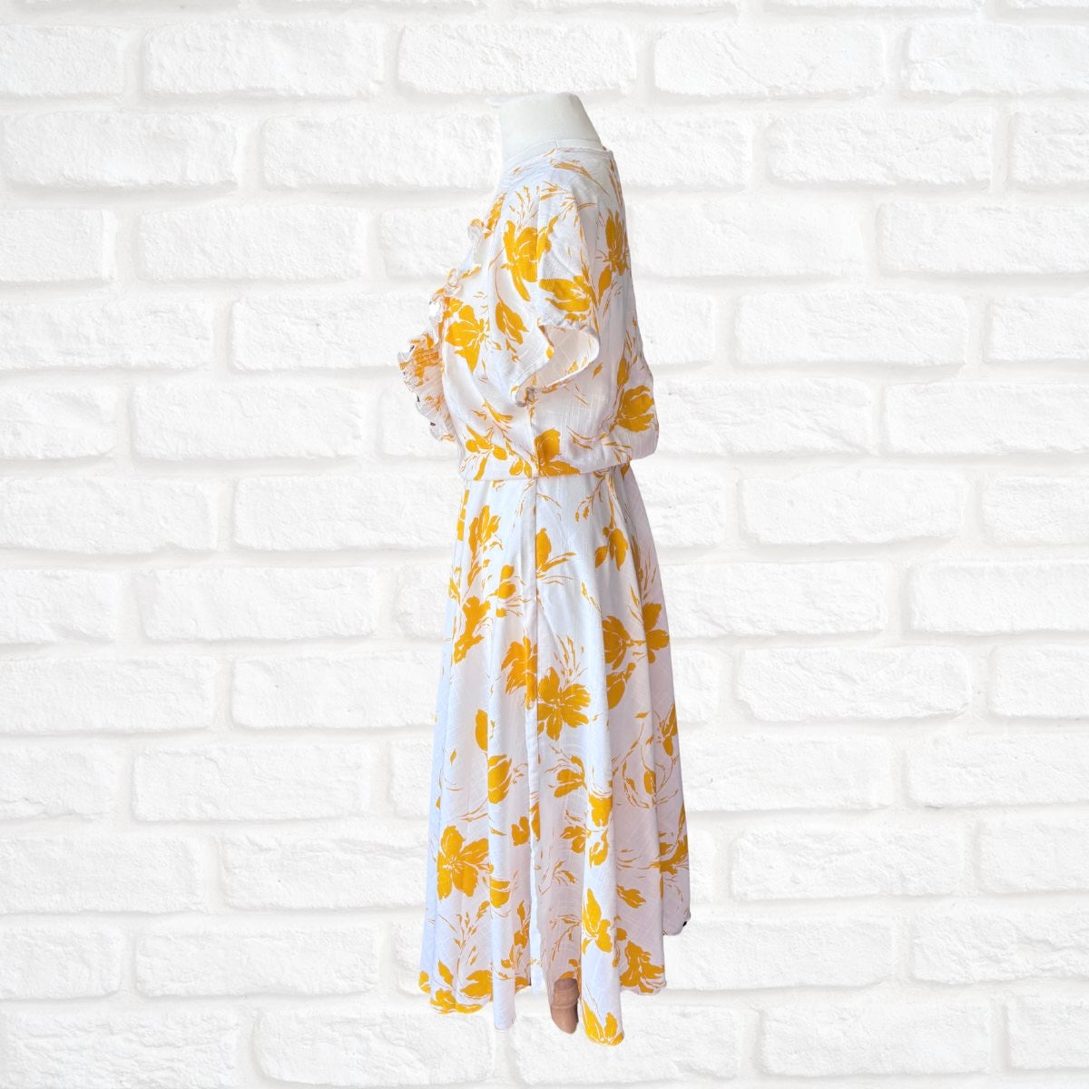 White dress with yellow floral pattern on a white brick wall background