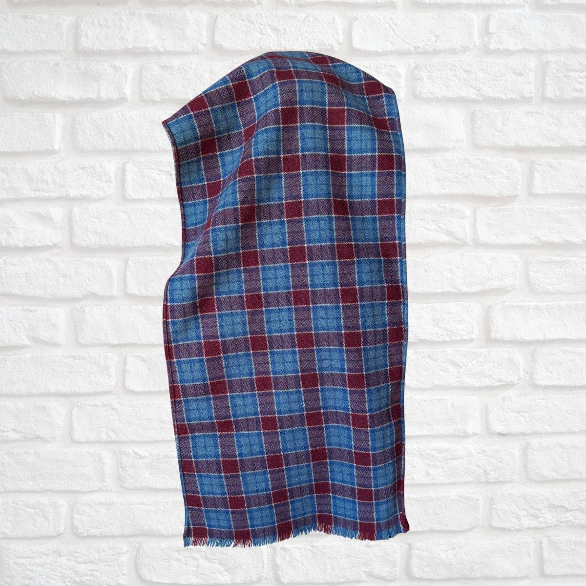 Plaid scarf  with blue and red pattern on a white brick wall background