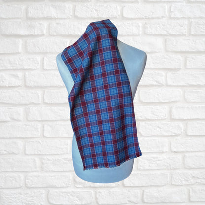 Blue and red plaid scarf on a mannequin against a white brick wall background
