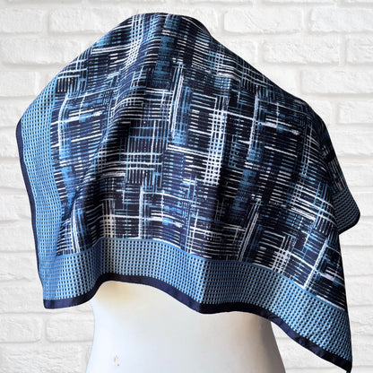 Blue and black patterned scarf on a mannequin against a white brick wall.