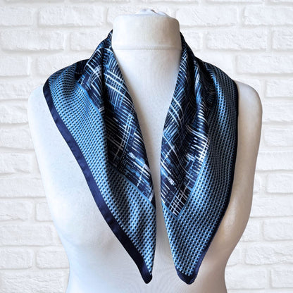 Mannequin wearing a blue and black patterned scarf against a white brick wall.