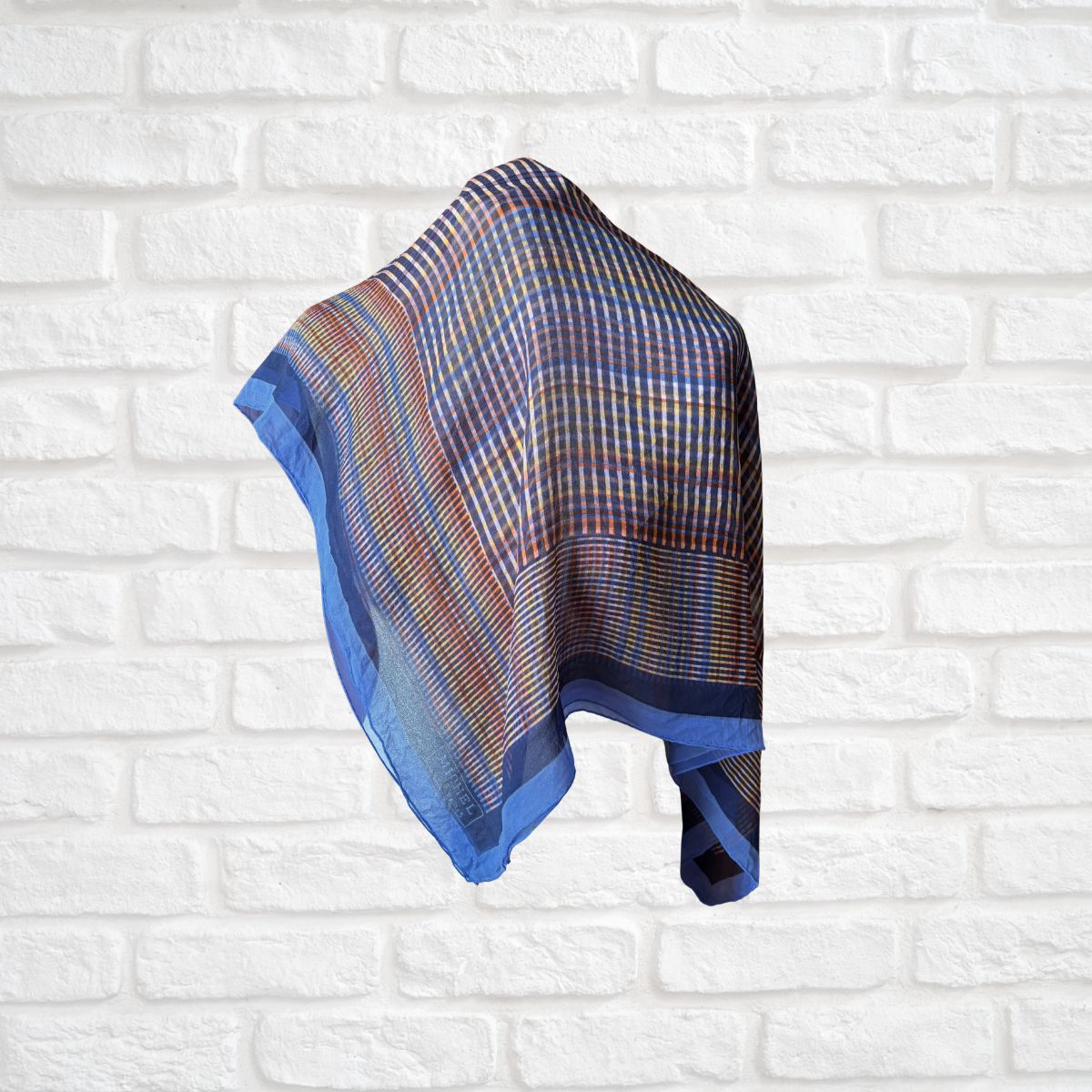 Colourful scarf with blue border on a white brick wall background