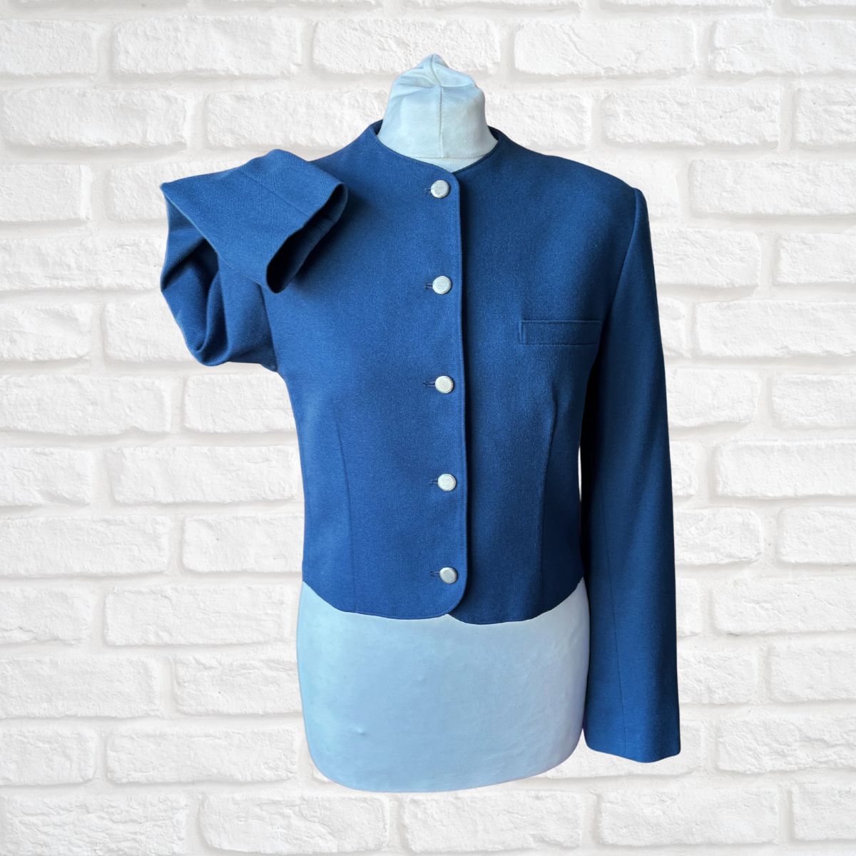 Blue jacket with silver  buttons on a mannequin against a white brick wall background