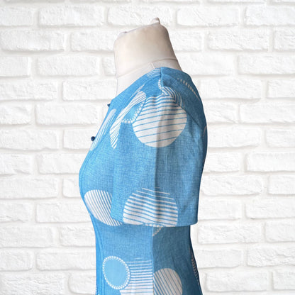 Blue dress  with white patterns on a mannequin against a white brick wall.