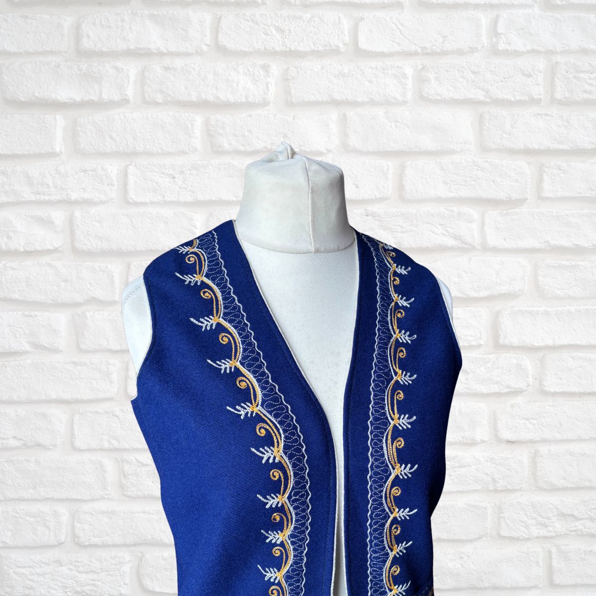 Blue embroidered vest on a mannequin against a white brick wall background
