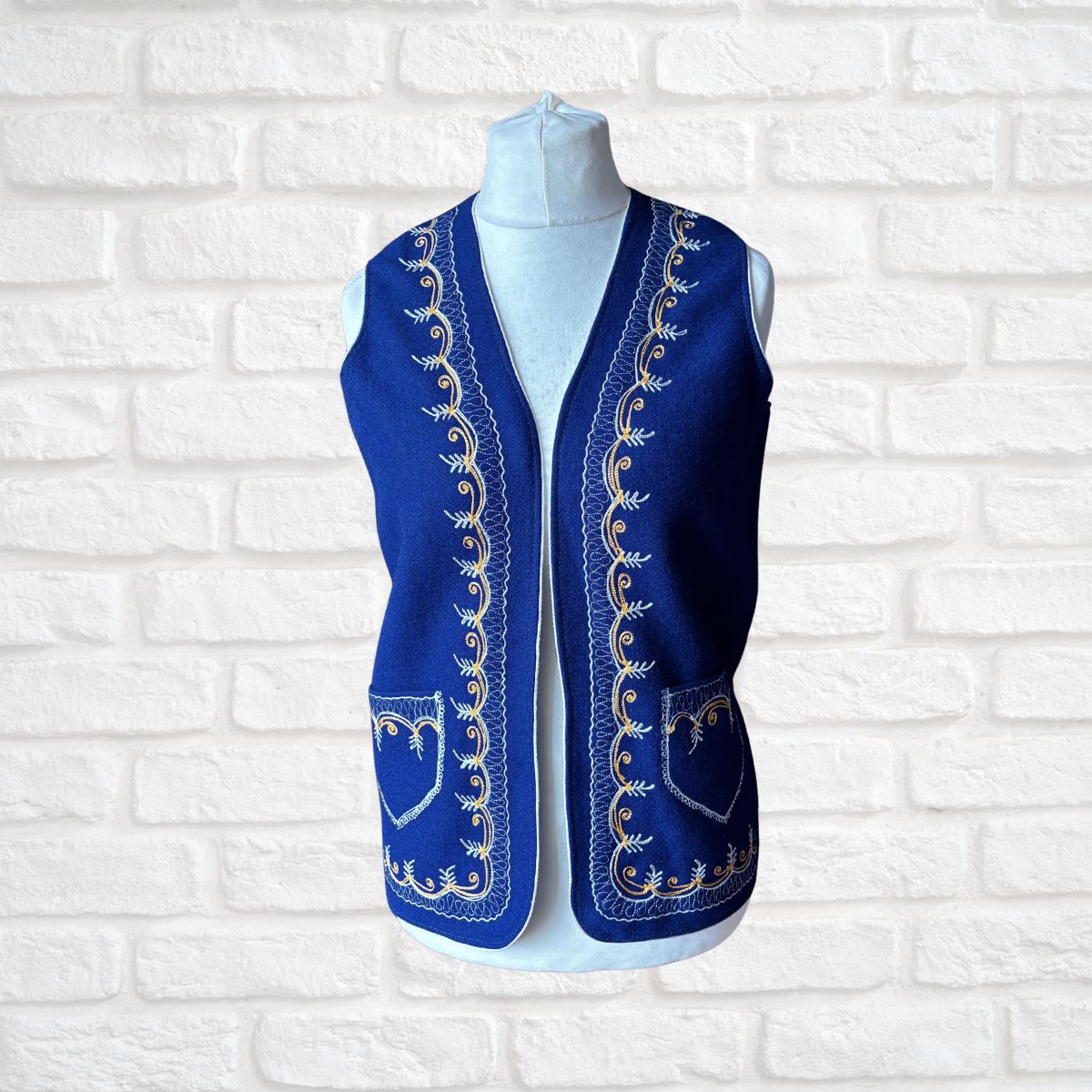 Blue embroidered vest on a mannequin against a white brick wall background