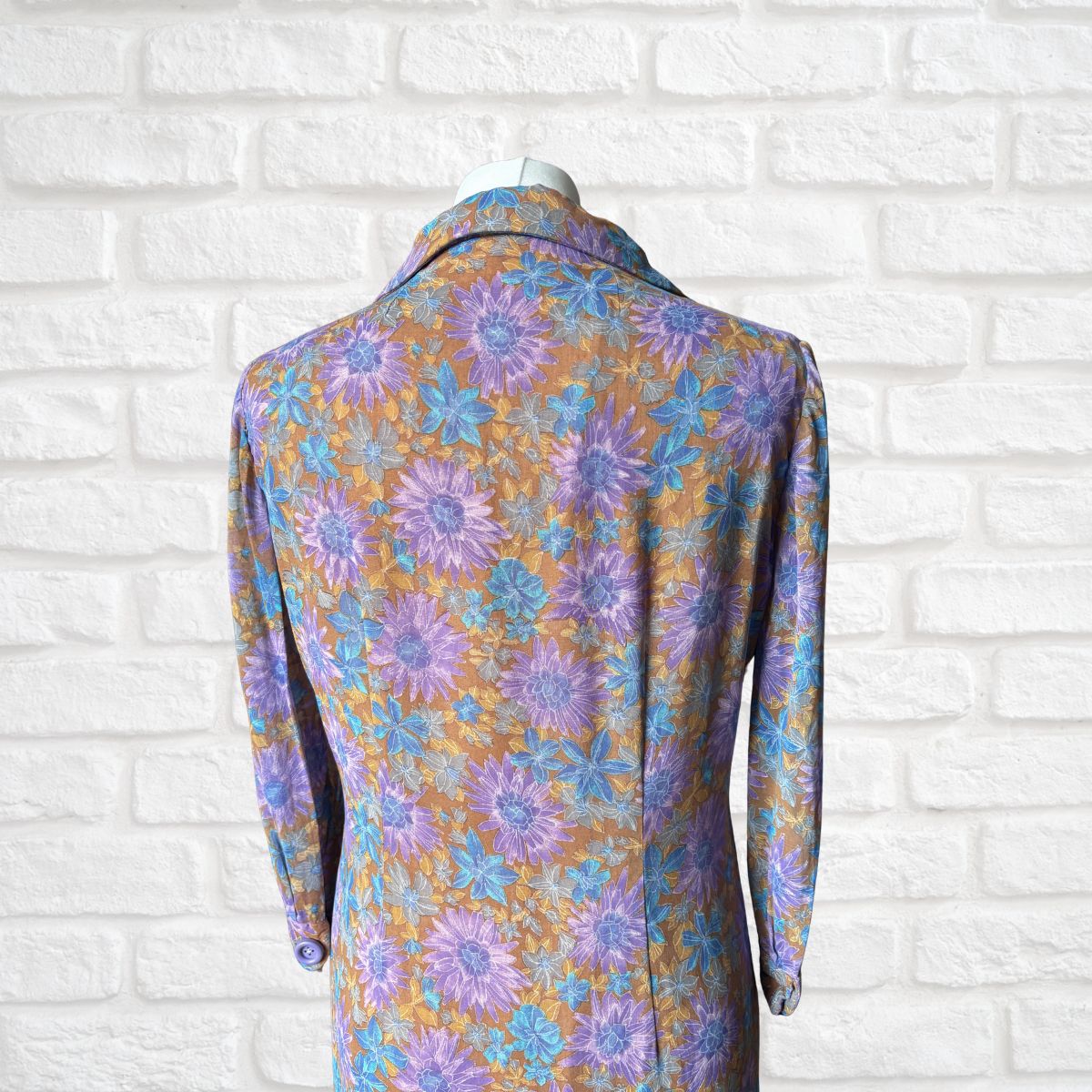 Floral patterned dress on a mannequin against a white brick wall.