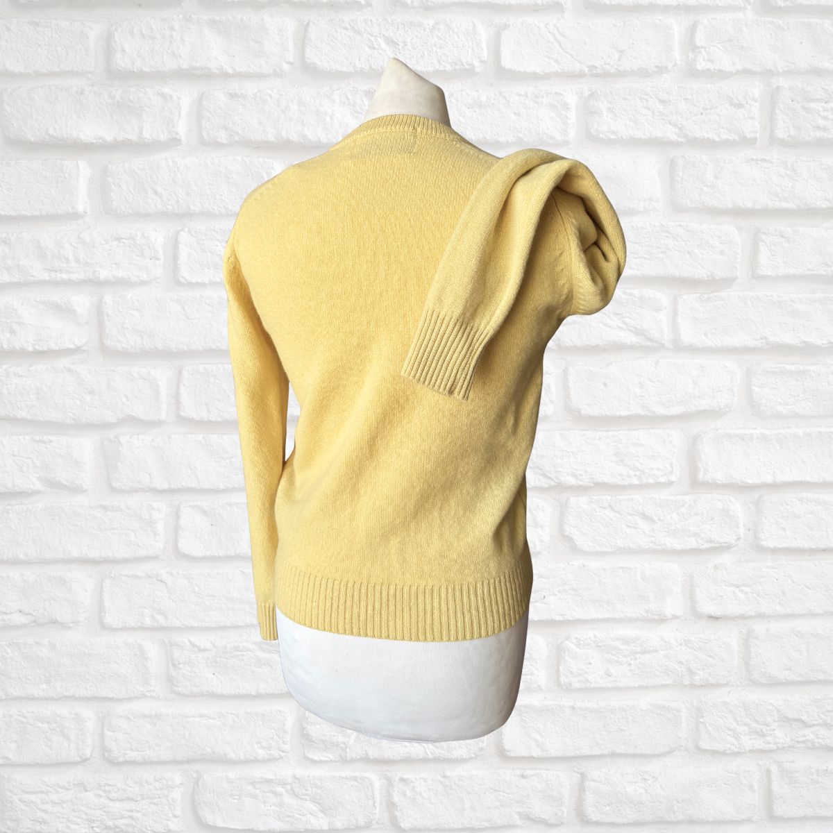 Yellow sweater on a mannequin against a white brick wall background