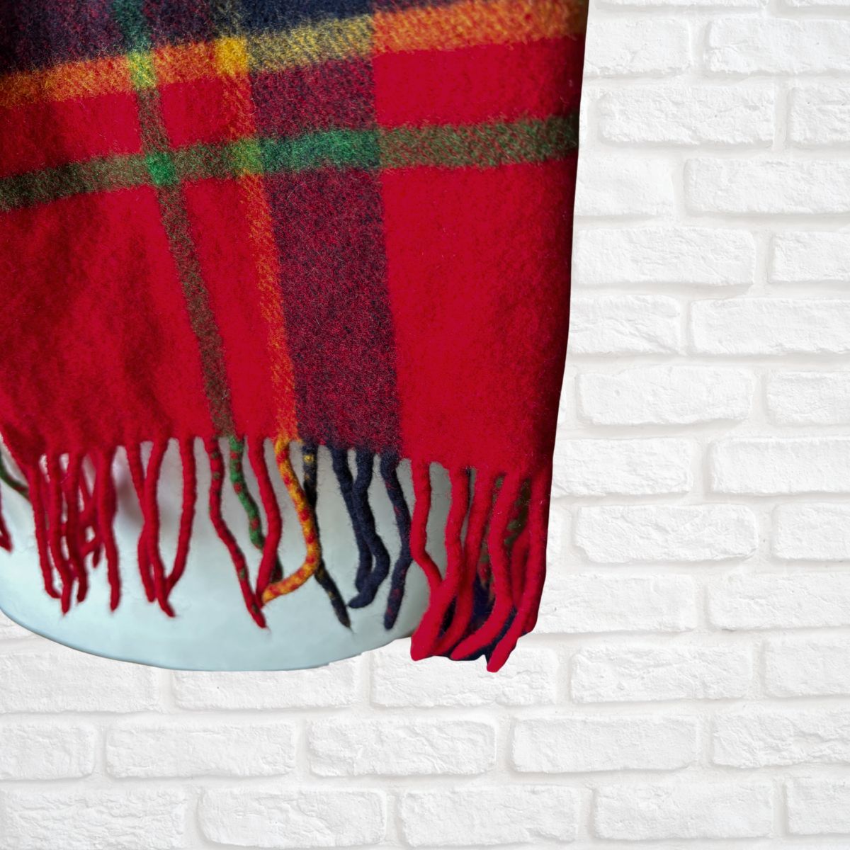 Plaid scarf with colourful pattern draped over a white brick wall.