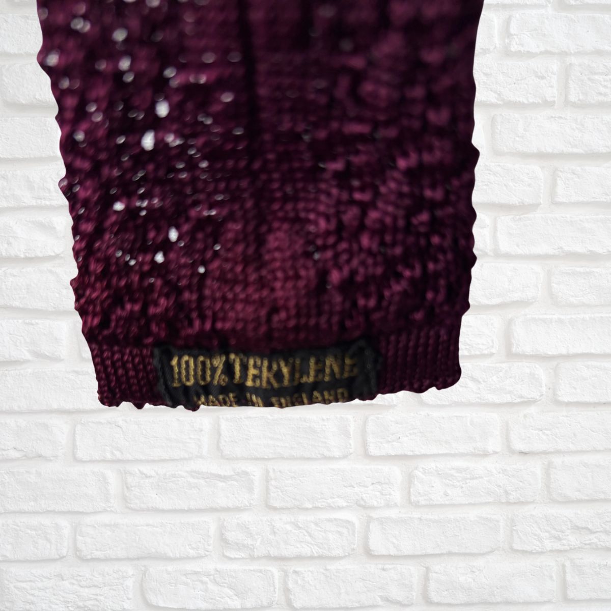 Close-up of a textured purple fabric with a label on a white brick wall background