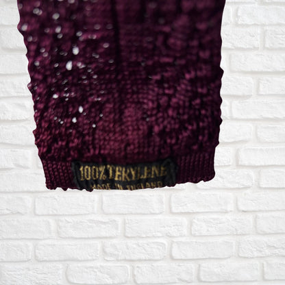 Close-up of a textured purple fabric with a label on a white brick wall background
