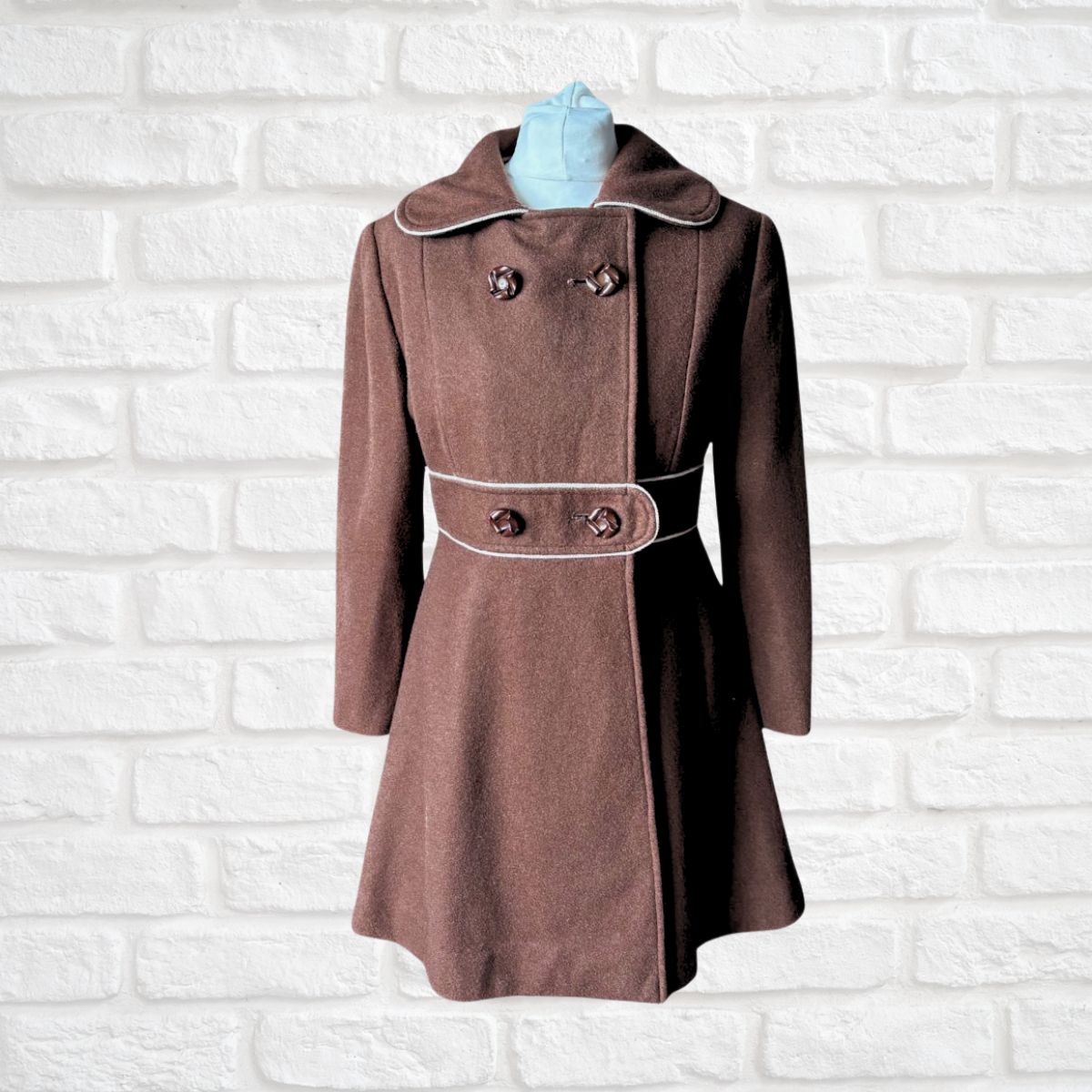 Brown coat with white trim on a white brick wall background