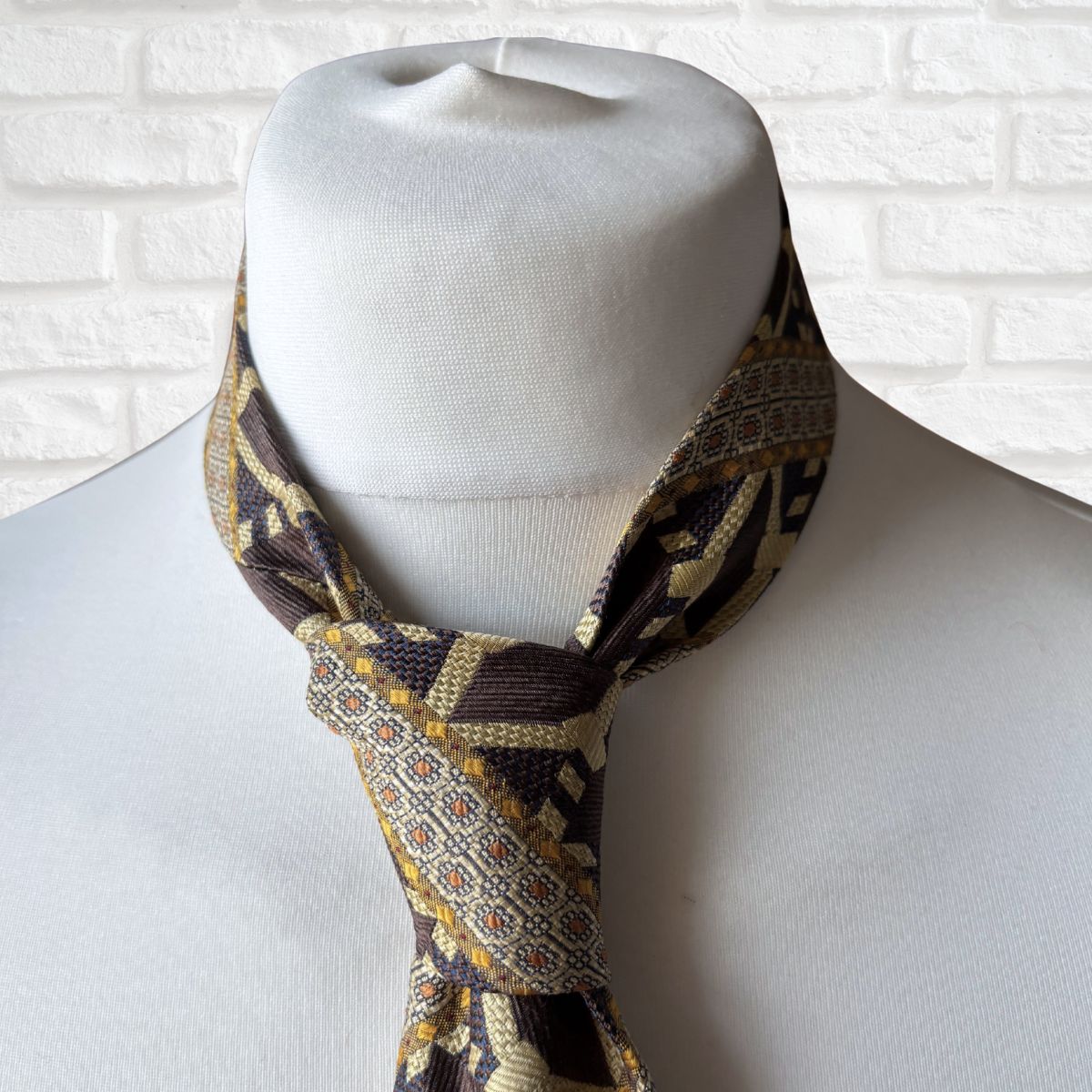 Patterned tie  on a mannequin against a white brick wall background