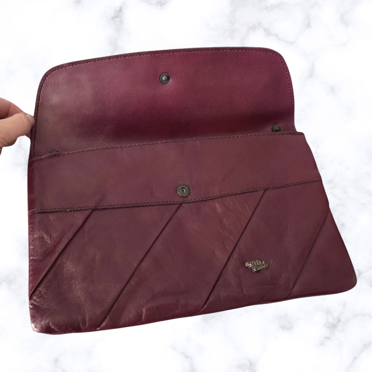 Maroon leather clutch bag held by a hand on a white background