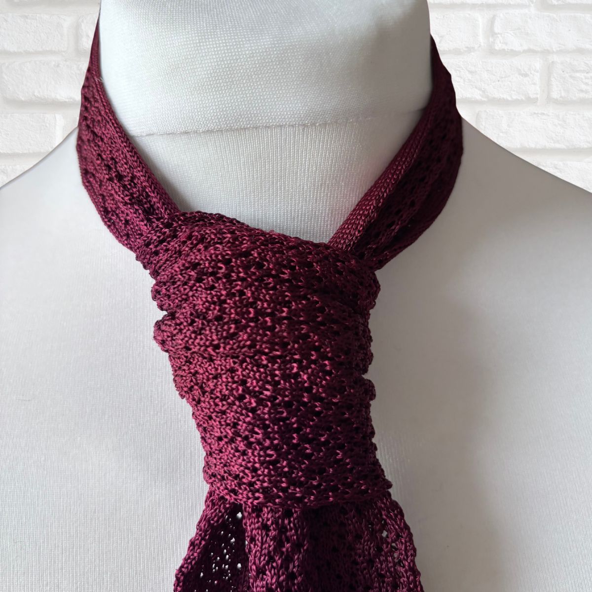 Maroon knitted scarf on a mannequin against a white brick wall.