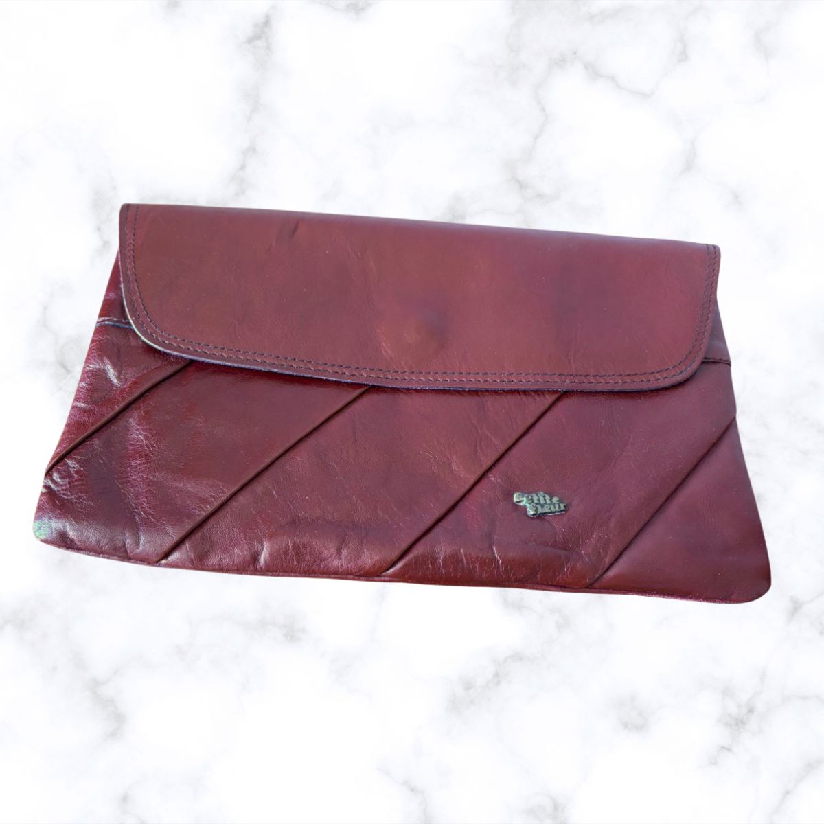 Maroon clutch bag on a white marble background
