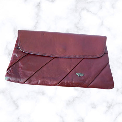 Maroon clutch bag on a white marble background