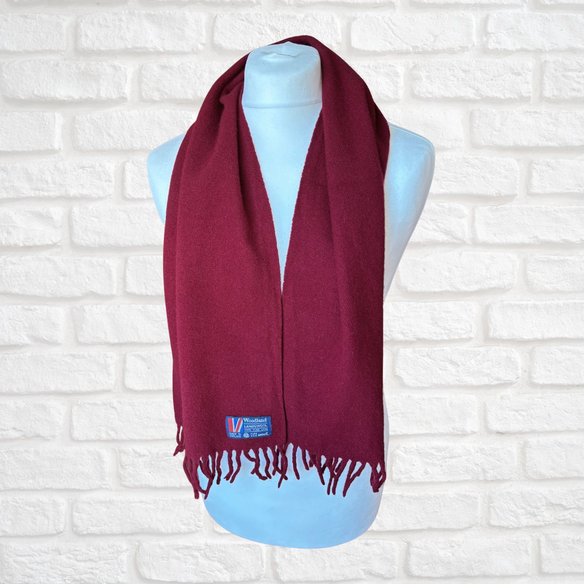 Maroon scarf on a mannequin against a white brick wall background