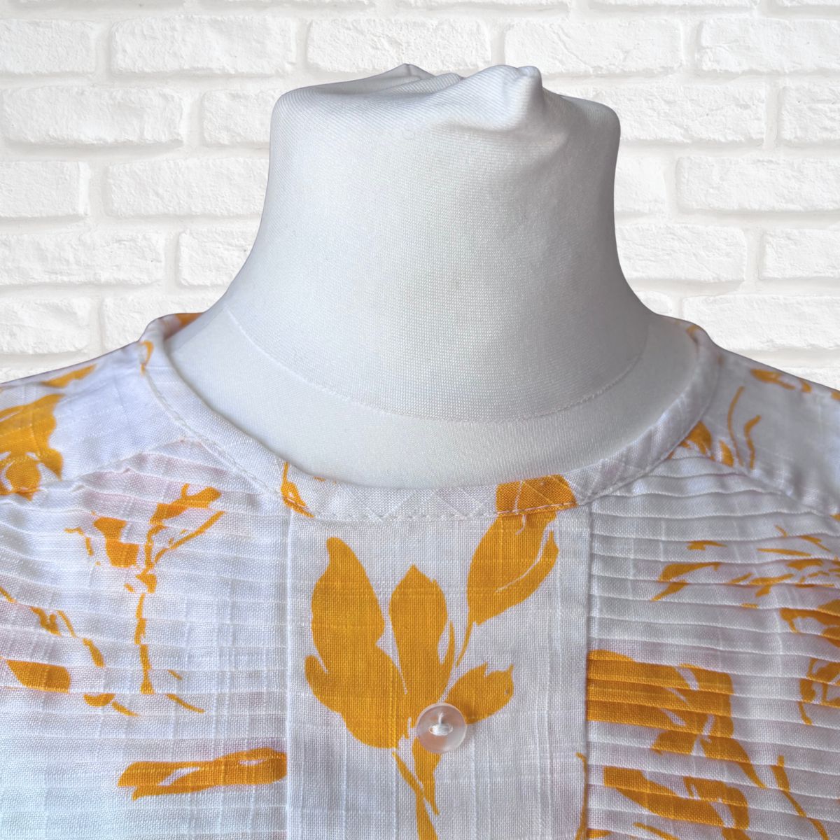 White dress with yellow  floral patterns on a mannequin against a white brick wall background