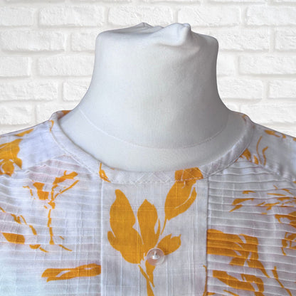 White dress with yellow  floral patterns on a mannequin against a white brick wall background