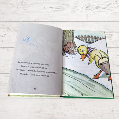 An open children's book lying on a white wood surface, showing a printed story page with text on the left and an illustrated winter scene with a duck on the right.