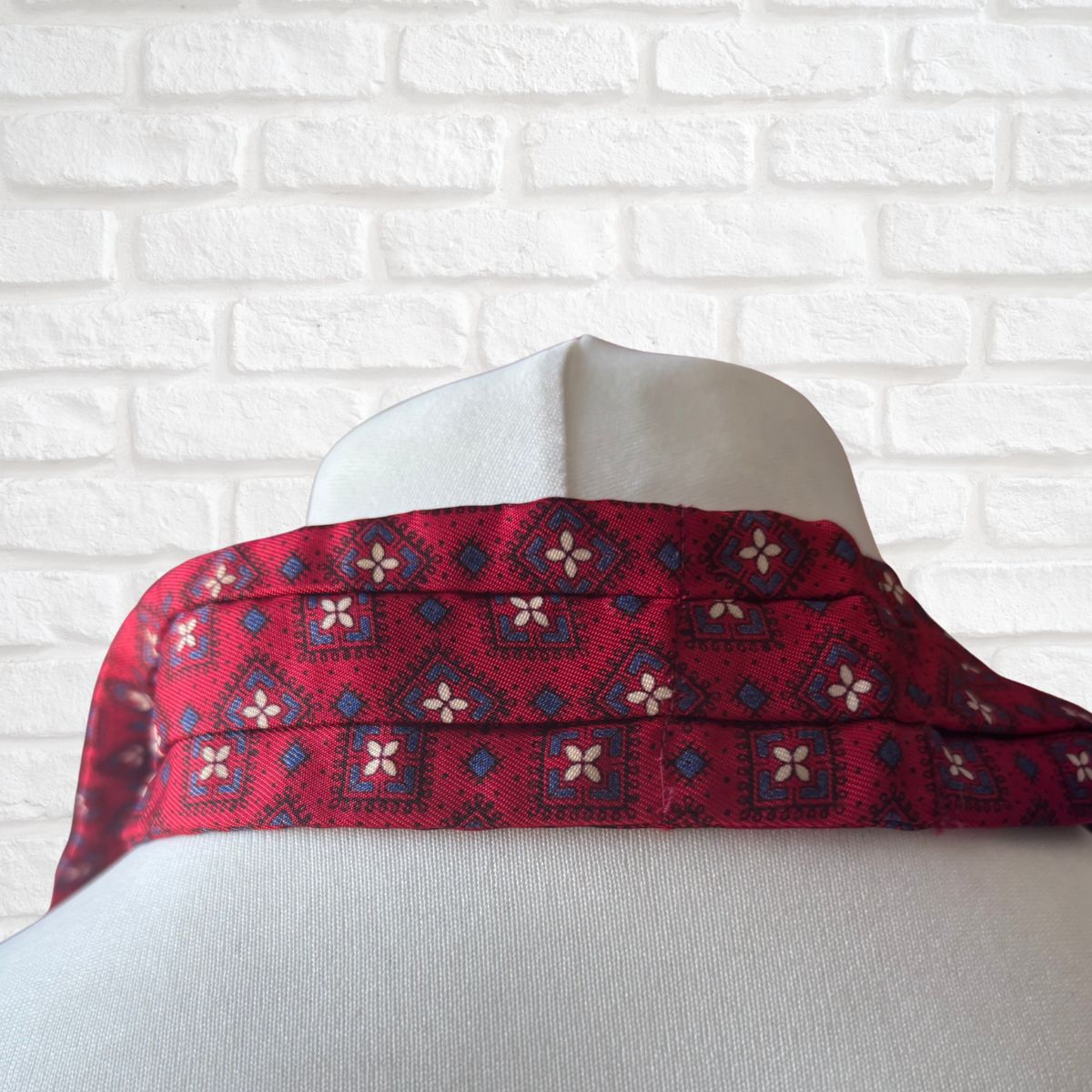Red patterned cravat draped over a mannequin against a white brick wall.