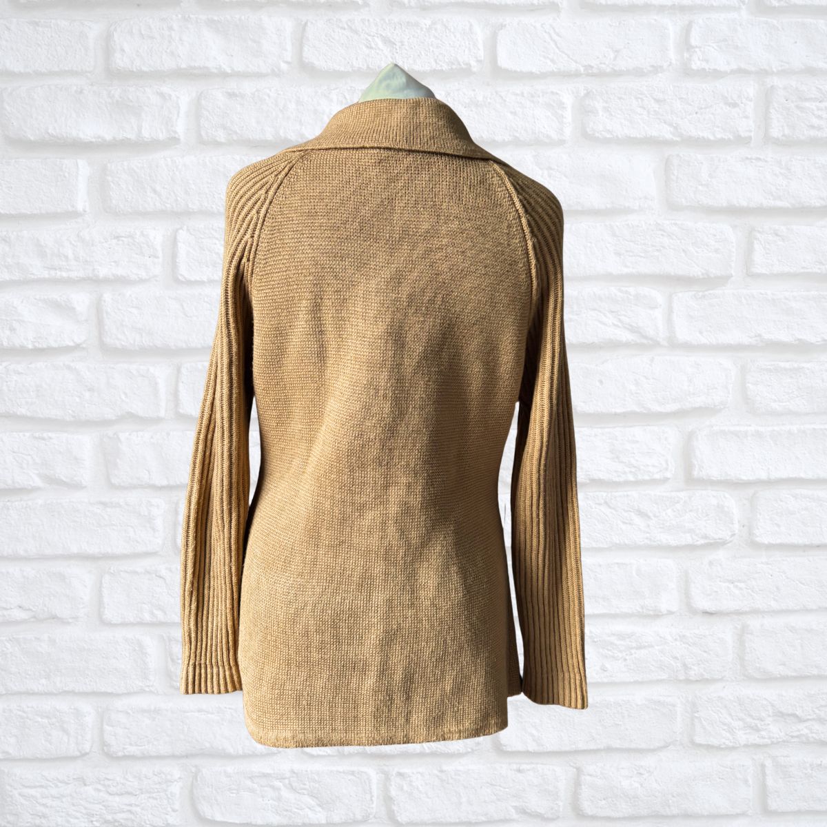 Beige knitted jacket on a mannequin against a white brick wall background