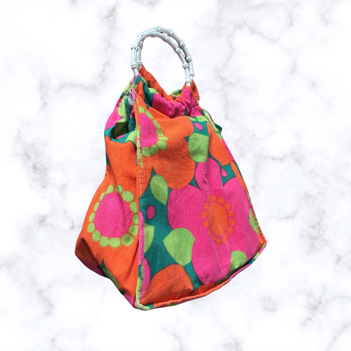 A top handle bag with a vibrant mid-century floral pattern in orange, pink, green, and teal, featuring a white twisted handle, set against a white marble background.